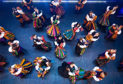 Widok z góry na scenę z Artystami w kostiumach ludowych w trakcie wykonywania choreografii tanecznej