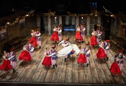Widok z góry na scenę na której znajdują się Artyści w kostiumach ludowych wraz z Parą Młodą w kostiumach krakowskich, w trakcie wykonywania choreografii tanecznej