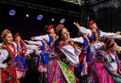 Grupa Artystów w kostiumach krakowskich na scenie w trakcie wykonywania choreografii tanecznej