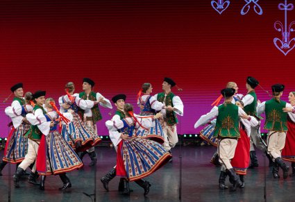 Pary Artystów w kostiumach spiskich w trakcie wykonywania choreografii tanecznej na scenie