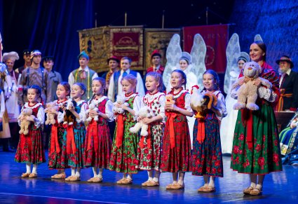 Grupa dziewczynek "Przedszkolaków" w kostiumach podhalańskich trzymajaca w rączkach pluszaki, obok nich Artystka również w kostiumie podhalańskim
