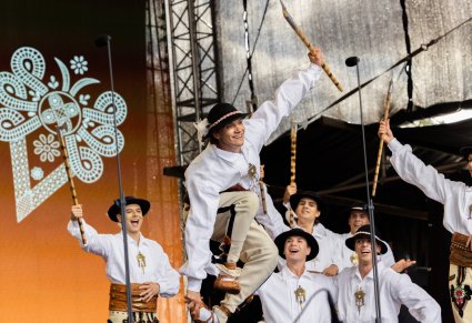 Grupa Artystów w kostiumach podhalańskich w trakcie wykonywania choreografii tanecznej
