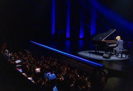 Na scenie fortepian na którym gra młody pianista, widoczny również orkiestron