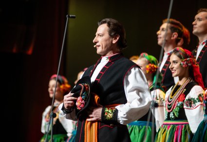 Zbliżenie na solistę chóru podczas koncertu z widocznych chórem w tle