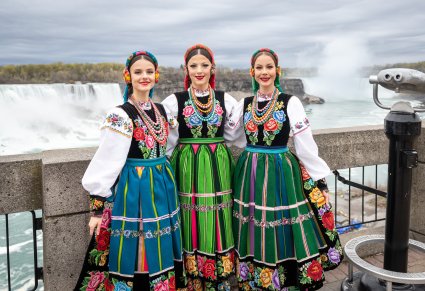 Trzy uśmiechnięte Artystki w kostiumach łowickich na tle wodospadu Niagara
