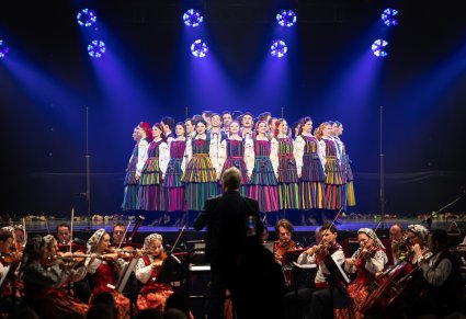 Na scenie Artyści w kostiumach opoczyńskich w trakcie wykonywania pierwszej choreografii tanecznej na koncercie, widoczna część orkiestry w kostiumach wilanowskich