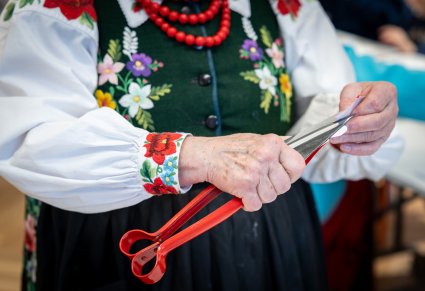 Zbliżenie na prowadzącą warsztat rękodzielniczy w trakcie wykonywania wycinanek dużymi nożycami