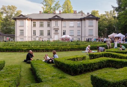 Na pierwszym planie uczestnicy IX Pikniku Rodzinnego z zespołem "Mazowsze" w czasie odpoczynku na trawniku przed Pałacem w Karolinie