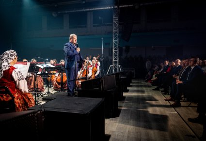 Dyrektor w trakcie wypowiedzi do mikrofonu, za nim część orkiestry w kostiumach wilanowskich