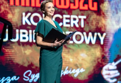 Konferansjerka w długiej, zielonej sukni na scenie