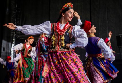 Grupa Artystów na pierwszym planie w kostiumach krakowskich wykonująca choreografię taneczna na scenie