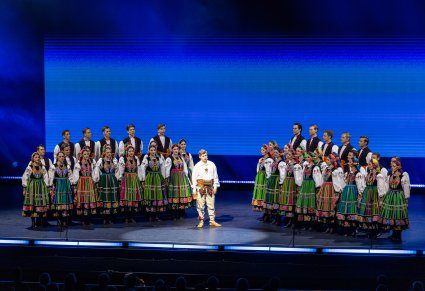Na środku sceny Solista w kostiumie podhalańskim a po jego bokach Artyści Chóru w kostiumach łowickich