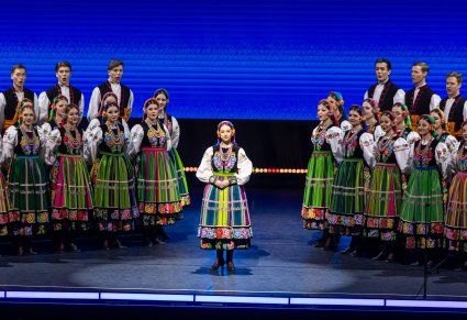 Na środku Solistka w kostiumie łowickim, po jej bokach Artyści Chóru również w kostiumach łowickich