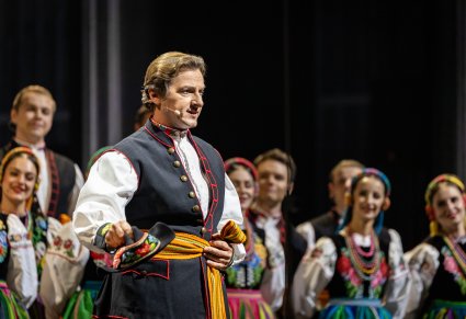 Zbliżenie na Solistę w kostiumie łowickim wykonującego utwór "Furman", w tle część Artystów Chóru