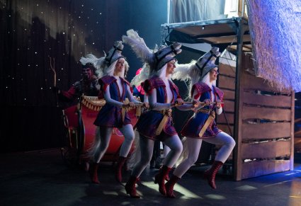 Widok na sanie ciągnięte przez Artystki w kostiumach koni, w saniach siedzi postać Diabła Ludowego