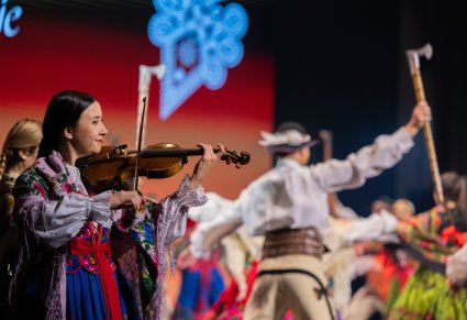 Na pierwszym planie Artystka z Orkiestry w kostiumie podhalańskim, grająca na skrzypcach