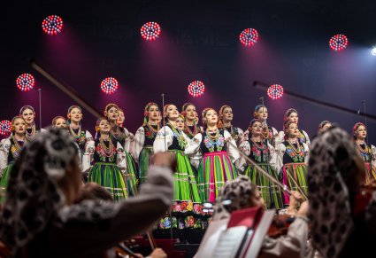 Na pierwszym planie Artystki Orkiestry w kostiumach wilanowskich grające na instrumentach smyczkowych, w tle na scenie na środku dwie Solistki w kostiumach wilanowskich, za nimi reszta część Chóru