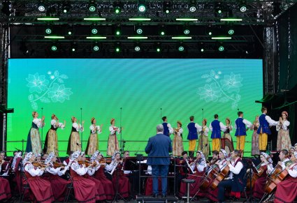 Na scenie Artyści baletu w kostiumach rozbarskich podczas wykonywania choreografii tanecznej, widoczna również orkiestra wraz z Dyrygentem