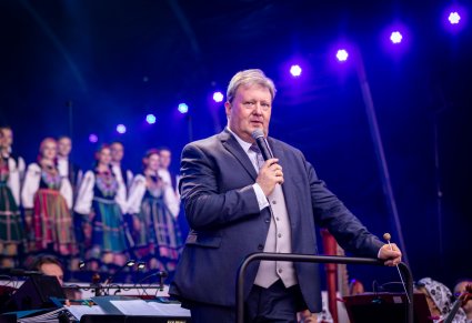 Na pierwszym planie Dyrektor Jacek Boniecki przemawiający do mikrofonu a w tle część Artystów w kostiumach łowickich