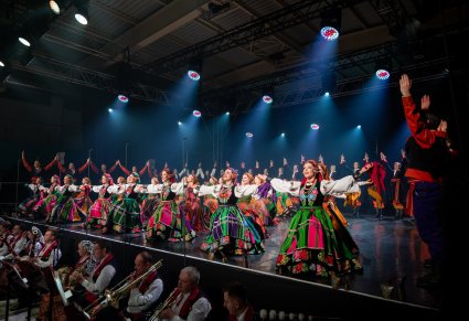 Na scenie Artyści w kostiumach ludowych podczas ukłonów, niżej część orkiestry w kostiumach wilanowskich