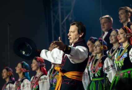 Zbliżenie na Solistę wykonującego utwór 'Furman", za nim widoczna część Artystów Chóru w kostiumach łowickich