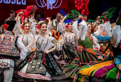 Zbliżenie na tancerki "Mazowsza" w kostiumach łowickich i tancerki baletu JOC w tradycyjnych kostiumach na scenie