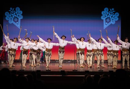 Grupa Artystów w kostiumach podhalańskich w trakcie wykonywania spektakularnej choreografii z wykorzystaniem ciupag
