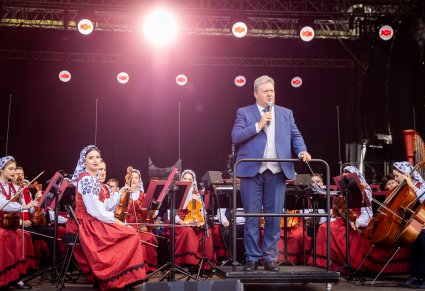 Dyrektor Jacek Boniecki w trakcie przemowy do mikrofonu, za nim orkiestra