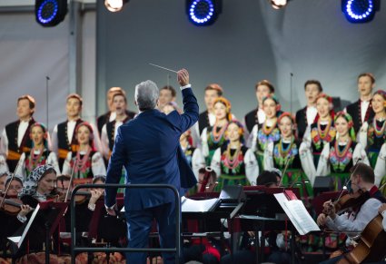 Dyrektor zespołu podczas dyrygowania, w tle orkiestra w kostiumach wilanowskich oraz chór w kostimach łowickich