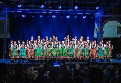 Chórzyści na scenie w kostiumach łowickich z widoczną publicznością