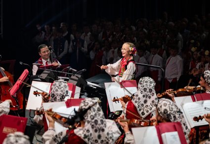 Zbliżenie na małą dziewczynkę w kostiumie ludowym, która dyryguje orkiestrze i chórowi
