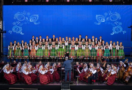 Na scenie Artyści chóru w kostiumach łowickich wraz z Artystami Orkiestry w kostiumach wilanowskich i Dyrygentem trzymającym w górze batutę