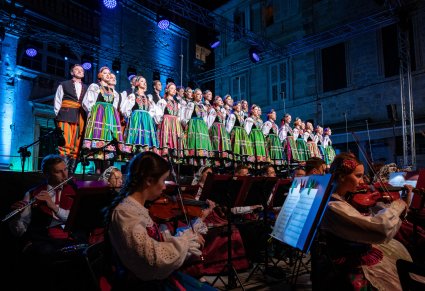 Na pierwszym planie Orkiestra smyczkowa a na drugim Artyści chóru w kostiumach łowickich