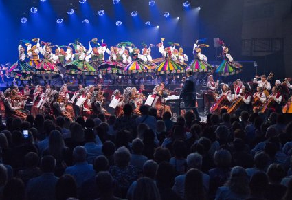 Widok na scenę na której znajdują się Artyści w kostiumach ludowych, niżej orkiestra w kostiumach wilanowskich