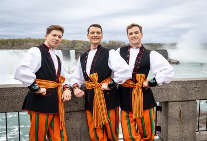 Trzech uśmiechniętych Artystów w kostiumach łowickich na tle wodospadu Niagara