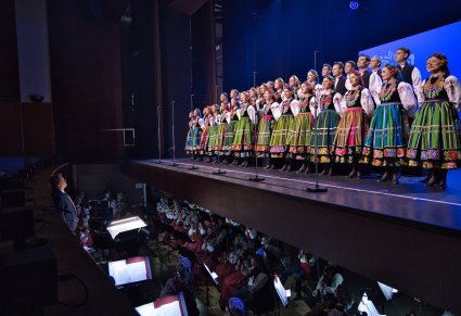 Na scenie Artyści chóru w kostiumach łowickich, niżej orkiestron w którym znajdują się Artyści orkiestry w kostiumach wilanowskich wraz z Dyrygentem