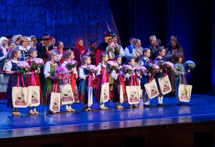 Na scenie najmłodsze Artystki trzymające w rękach torby z prezentami i kwiaty, w tle reszta część Artystów występująca w widowisku