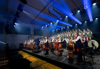 Widok na scenę na której znajdują się Artyści Orkiestry w kostiumach wilanowskich wraz z Dyrygentem oraz Artyści Chóru w kostiumach łowickich