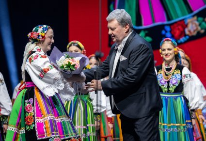 Dyrektor zespołu otrzymujący kwiaty od Publiczności, w tle Artyści w kostiumach łowickich