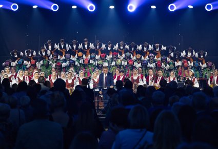 Na pierwszym planie Dyrygent zwrócony w stronę Publiczności , za nim Orkiestra w kostiumach wilanowskich oraz kłaniający się Chór w kostiumach łowickich