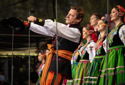 Zbliżenie na Solistę w kostiumie łowickim wykonującego utwór "Furman", w tle widoczna część Artystów chóru w kostiumach łowickich