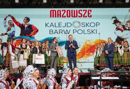 Na scenie Dyrektor zespołu "Mazowsze" wraz z merem rejonu selecznickiego oraz przedstawiciele Samorządu Województwa Mazowieckiego, w tle Artyści w kostiumach łowickich