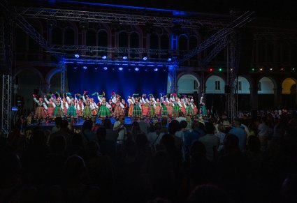Grupa tancerzy w kostiumach łowickich występuje na oświetlonej scenie podczas nocnego koncertu plenerowego przed publicznością.