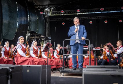Dyrektor Jacek Boniecki, który wygłasza mowę do mikrofonu, w tle orkiestra