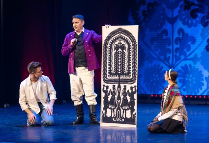 Na scenie Pan Kajetan trzymający wycinankę Kurpiowską a obok niego siedzący Tomek i Agnieszka