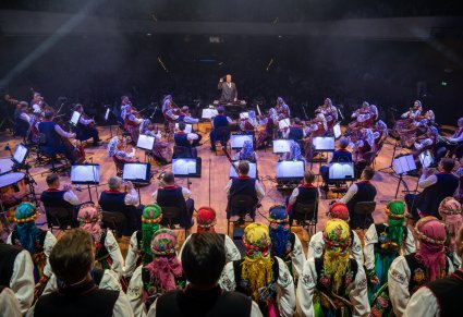 Na pierwszym planie Dyrektor zespołu "Mazowsze" zwrócony w stronę Orkiestry  i Chóru