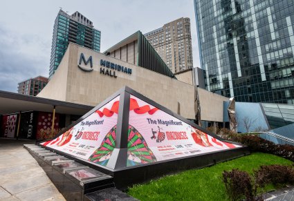 Zewnętrzny ekran reklamowy w kształcie piramidy, na ekranach widoczna informacja o koncercie Mazowsza w Meridian Hall. W tle widać budynek w którym odbywał się koncert