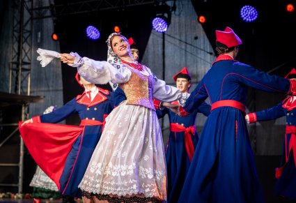 Artyści na scenie w kostiumach wilanowskich, Artystka odwraca się w stronę publiczności i macha białą chusteczką