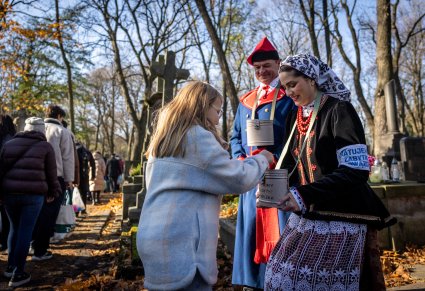 Dziewczynka wrzuca datki do puszki pary Artystów w kostiumach wilanowskich na Starych Powązkach