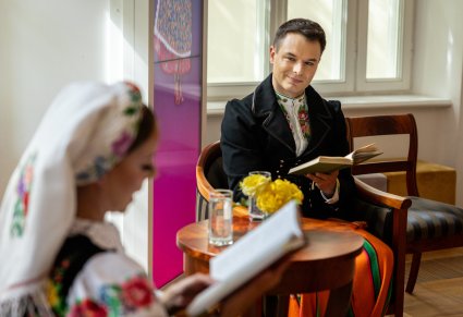 Artysta w kostiumie kocierzewskim, spogladający na czytającą koleżanke z zespołu
